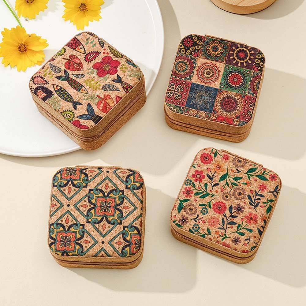 Vier quadratische Korkuntersetzer mit farbenfrohen floralen und geometrischen Mosaikmuster auf einer hellen Tischplatte angeordnet.