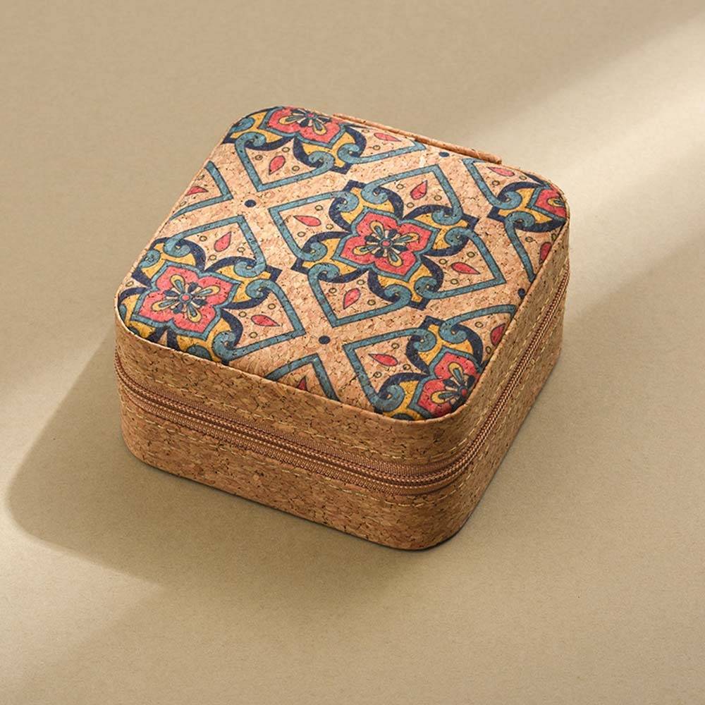 Kleine quadratische Korkfallverschlusstasche mit einem bunten geometrischen Blumenmuster auf dem Deckel, dargestellt auf einer einfachen beigen Oberfläche.