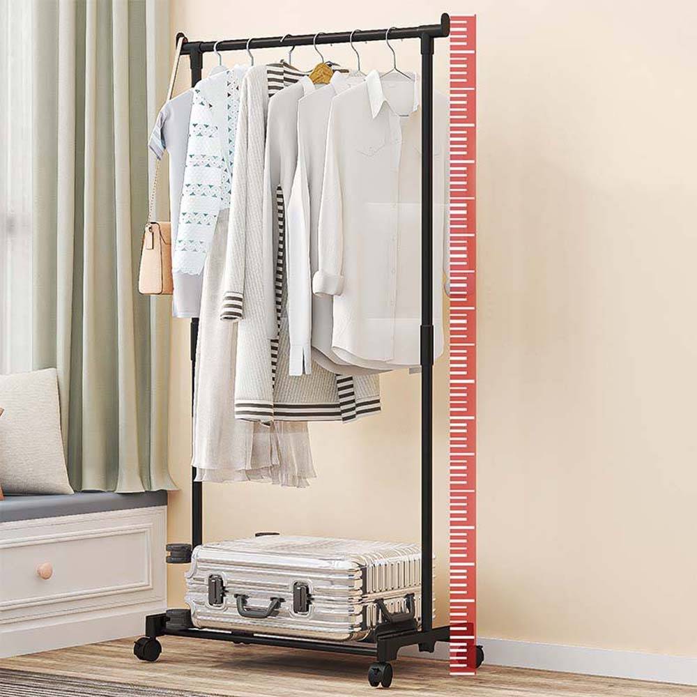 Kleidung auf einem rollbaren Kleiderständer neben einer roten Höhenskala, mit einem Koffer auf dem unteren Regal in einem Schlafzimmer.