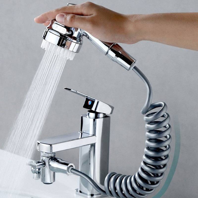 Eine Hand, die einen verchromten Duschkopf hält, sprüht Wasser über einen modernen Badewannenhahn mit einem aufgerollten Schlauch.