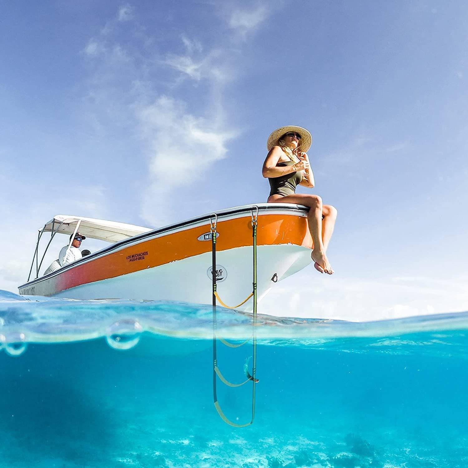 Eine Frau in einem Sonnenhut sitzt auf dem Bug eines kleinen Motorboots über klarem türkisblauem Wasser, wobei die Leiter des Bootes unter der Wasseroberfläche sichtbar ist.