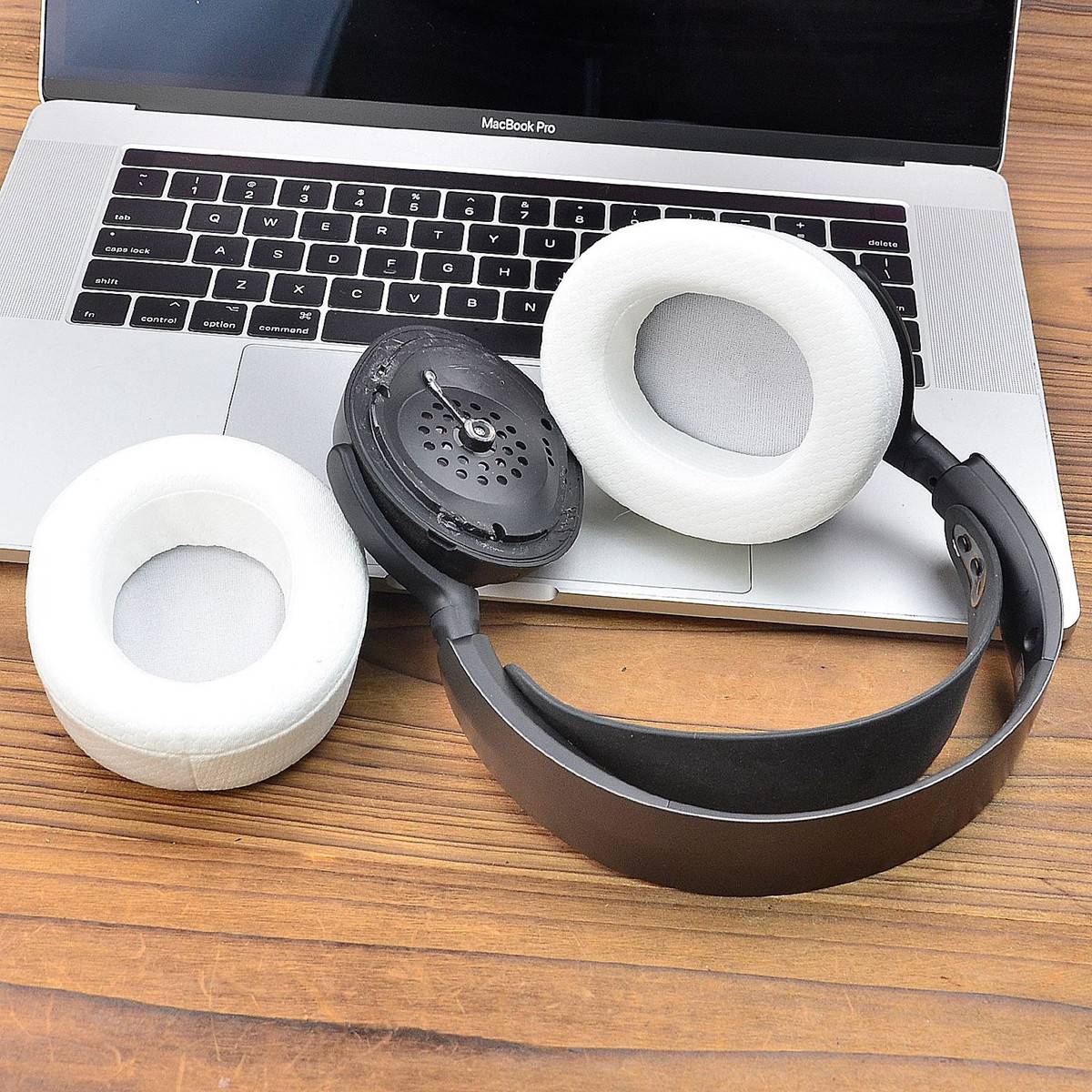 Zwei Ersatz-Ohrpolster und ein schwarzes Kopfband für Over-Ear-Kopfhörer liegen auf einer MacBook-Pro-Tastatur und einem Holzschreibtisch.