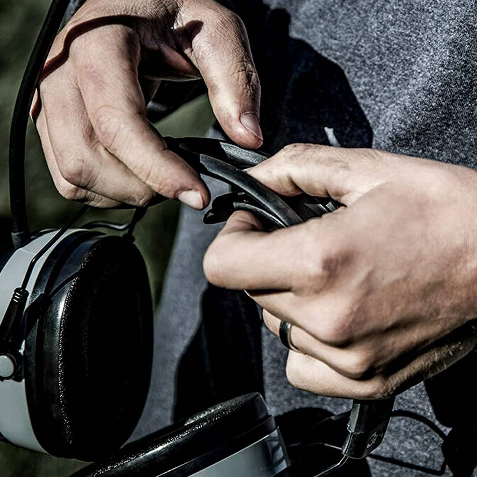 Nahaufnahme von Händen, die ein Kabel an Over-Ear-Kopfhörern einstellen, wobei die Kopfhörer gegen eine Person in einem dunklen Hemd ruhen.