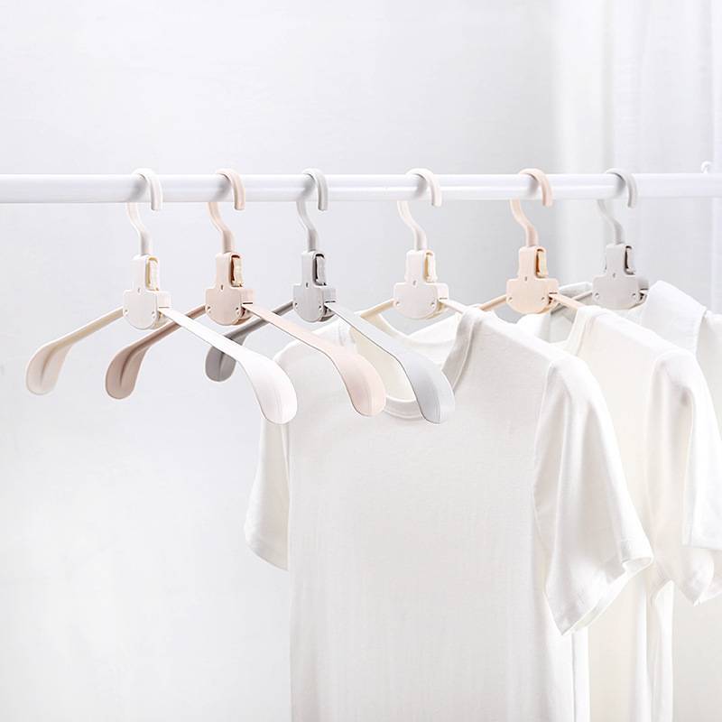 Mehrere weiße T-Shirts hängen auf pastellfarbenen Bügeln an einem Kleiderständer vor einem hellweißen Hintergrund.