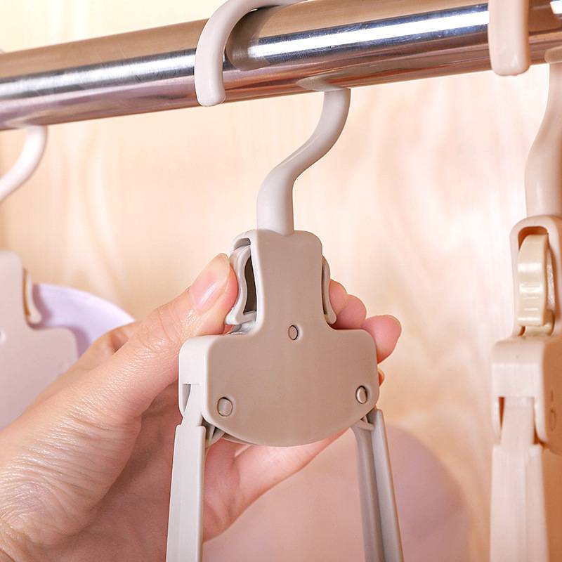 Hand, die einen beigen Kunststoff-Klemmhaken hält, der an einer Metallstange in einem Kleiderschrank befestigt ist, zeigt einen verstellbaren Kleiderorganizer.