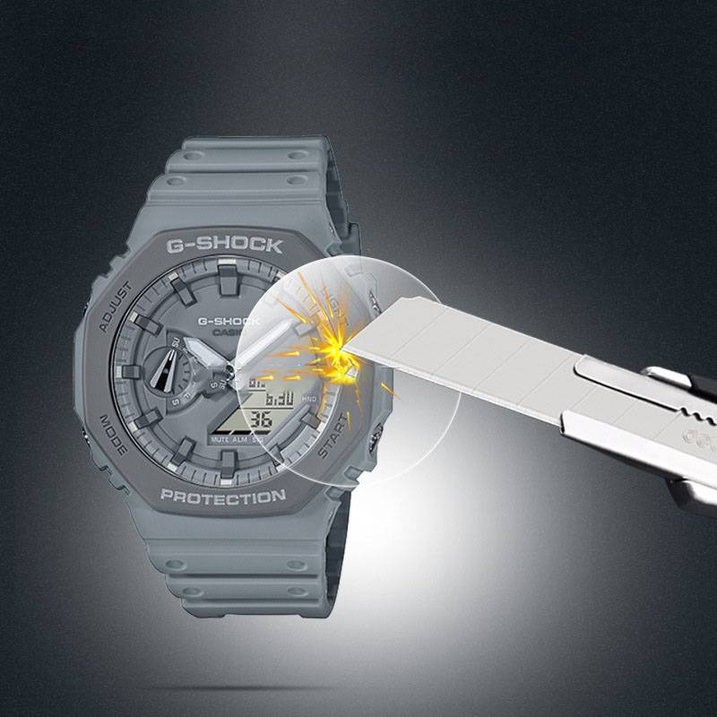Graue G-SHOCK-Armbanduhr, die zeigt, wie sie einer Utility-Messerklinge widersetzt, die auf das Kristallglas trifft, und damit Stoßfestigkeit und Haltbarkeit veranschaulicht.