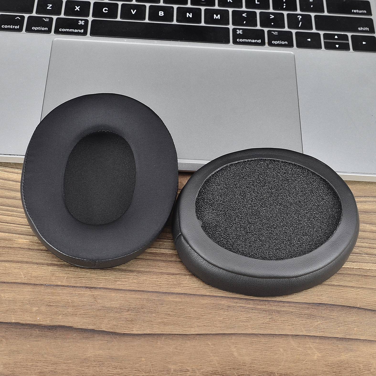 Zwei schwarze ovale Ohrpolster sitzen auf einem Holzschreibtisch vor einer Laptop-Tastatur und einem Trackpad.