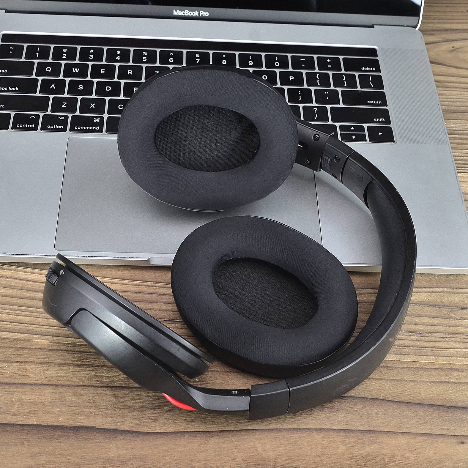 Schwarze Over-Ear-Kopfhörer ruhen auf einer silbernen MacBook-Pro-Tastatur auf einem Holzschreibtisch.