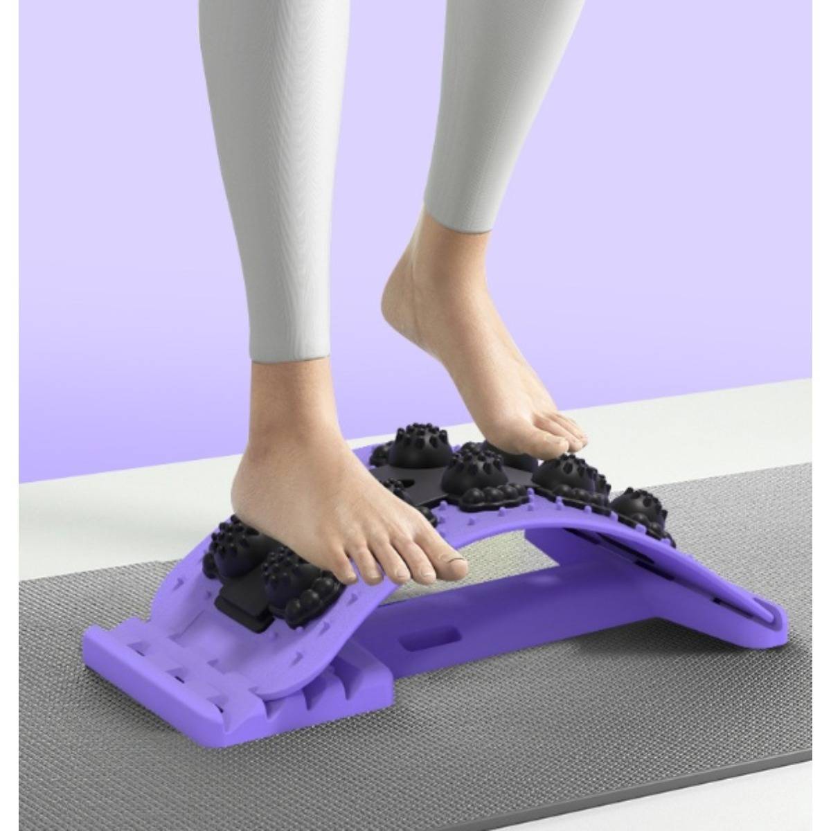 Eine Person verwendet einen lila gewölbten Fußmassager mit schwarzen Noppen und drückt dabei beide nackten Füße darauf, während sie auf einer Matte steht.