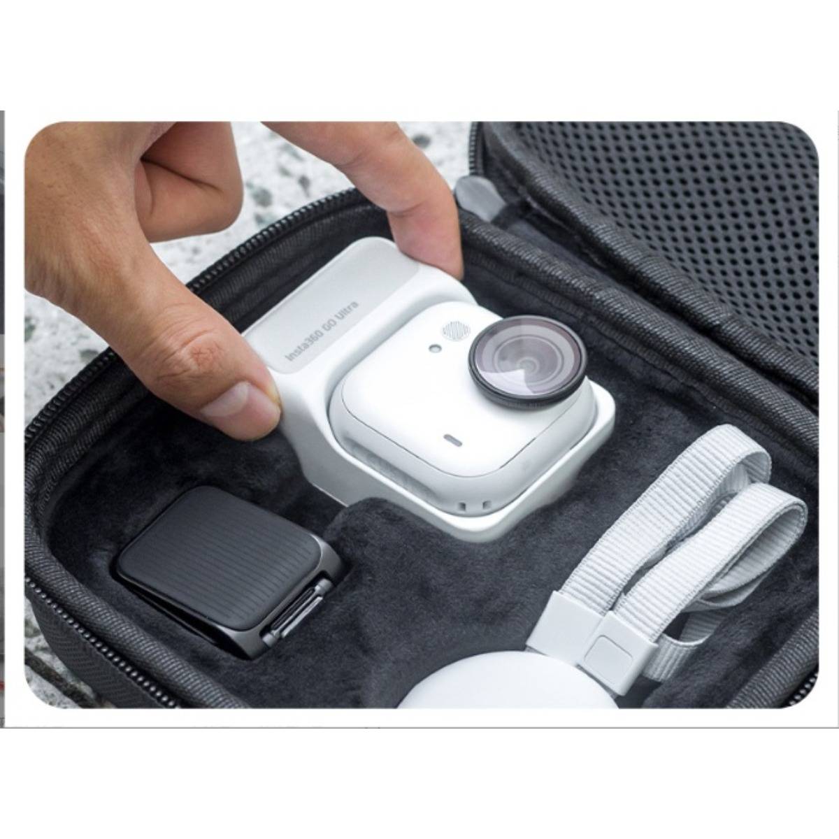 Eine Hand legt eine kleine weiße Action-Kamera in eine gepolsterte Transporttasche neben ein schwarzes Zubehör und einen weißen Gurt.