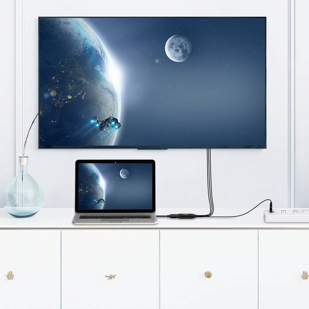 Wandmontierter Fernseher und Laptop zeigen die gleiche Weltraumszene mit Erde und Mond auf einem weißen Schreibtisch in einem minimalistischen Raum an.