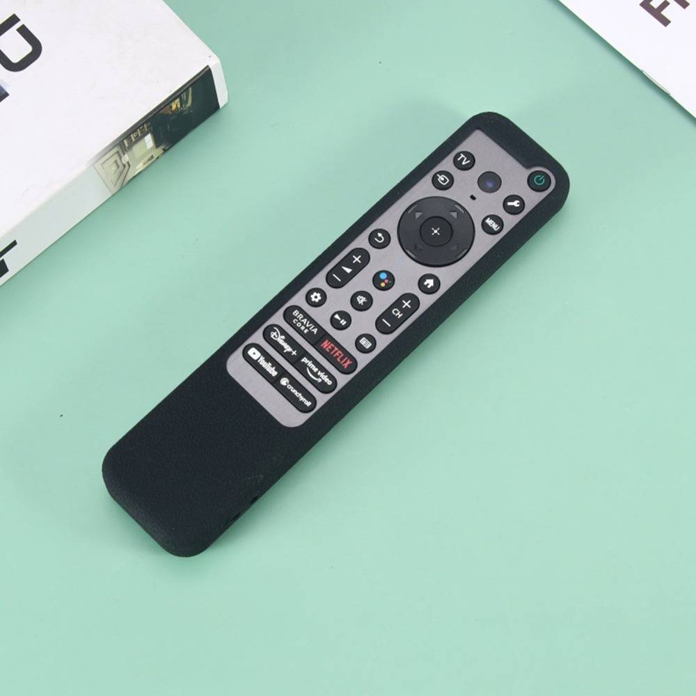 Schwarze Fernbedienung für den Fernseher mit vielen Tasten auf einer mintgrünen Oberfläche, neben einer Produktkartonecke abgebildet.
