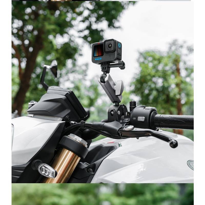 Actionkamera auf einem Motorradlenker montiert, am Spiegelbereich befestigt und nach vorne ausgerichtet, mit unscharfen Bäumen im Hintergrund.
