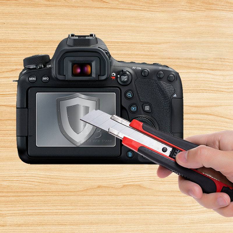 Eine Hand, die ein Universalmesser hält, schneidet über einen DSLR-Kamerabildschirm, auf dem ein Schildsymbol zu sehen ist, was auf Gerätesicherheit oder -schutz hindeutet.
