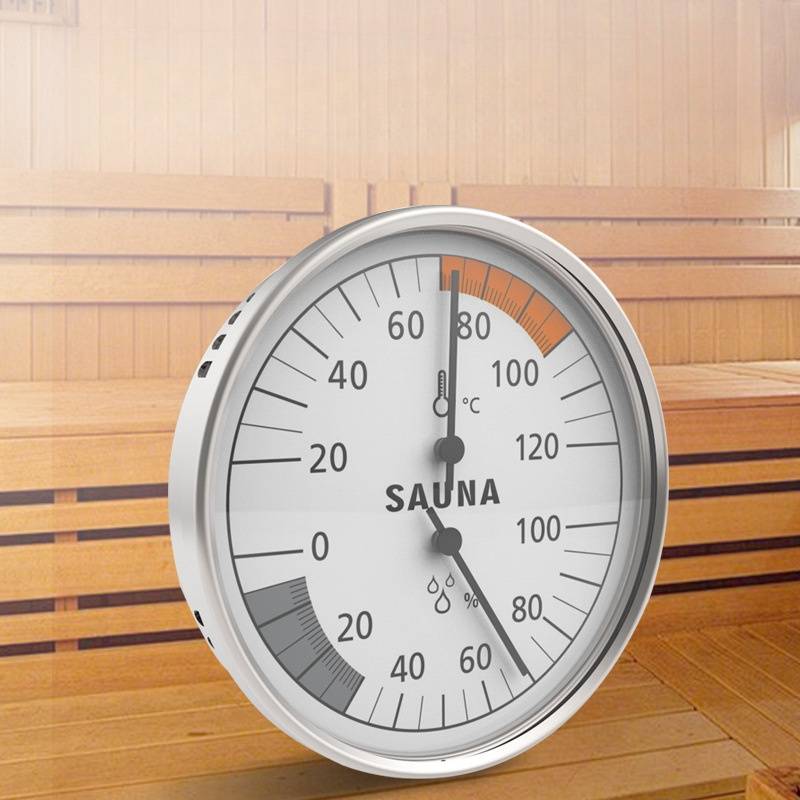 Analoges Sauna-Thermometer-Hygrometer auf einer Holzbank, zeigt etwa 80°C und 80% Luftfeuchtigkeit in einer Sauna.