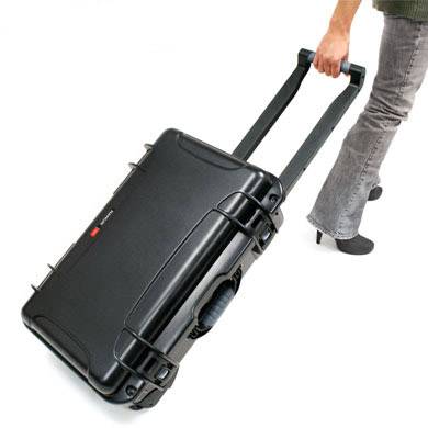 Eine Person zieht einen schwarzen Rollkoffer an seinem ausgefahrenen Griff vor weißem Hintergrund.