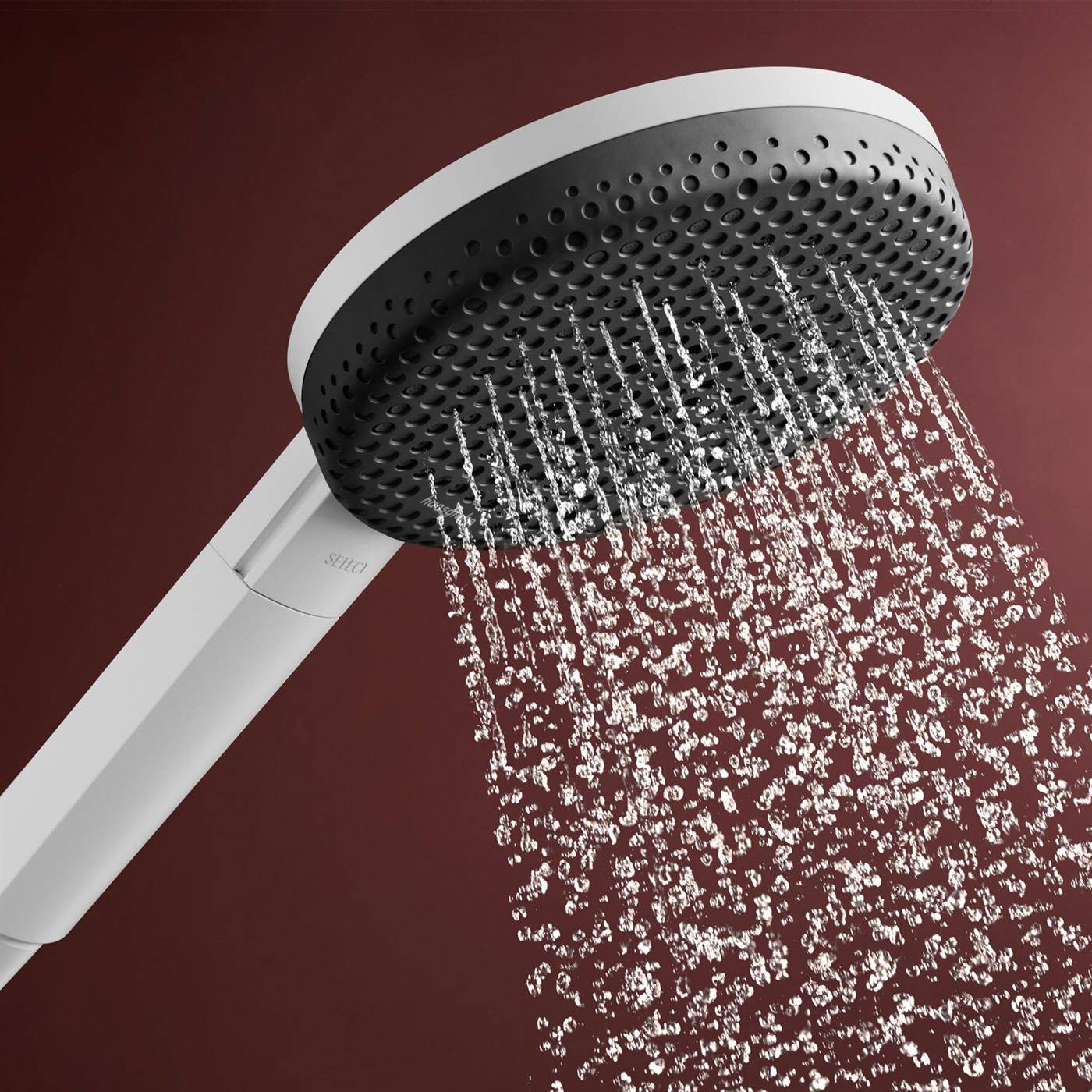 Handbrause mit Wasserstrahlen, die aus einer schwarzen kreisförmigen Fläche gegen einen dunkelroten Hintergrund spritzen.