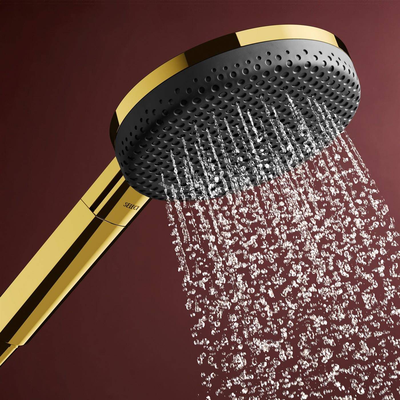 Goldene tragbare Duschkopf sprüht Wasser vor dunklem Burgundundergrund.