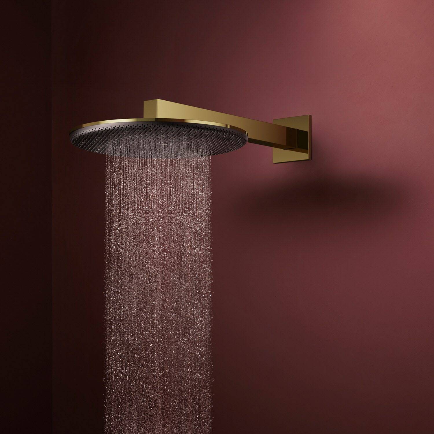 Goldener, wandmontierter Regenbrausekopf sprüht Wasser gegen eine dunkelbordeauxfarbene Wand
