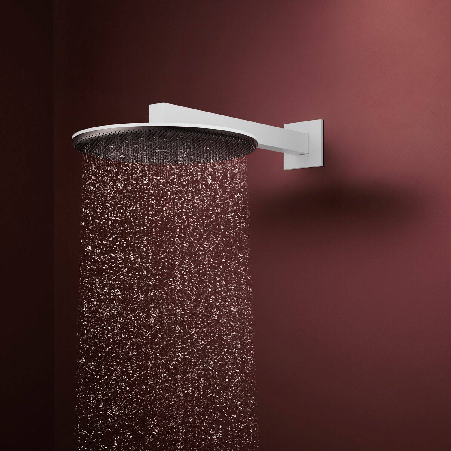 Ein an der Wand montierter runder Duschkopf sprüht Wasser gegen einen dunkelroten Hintergrund.