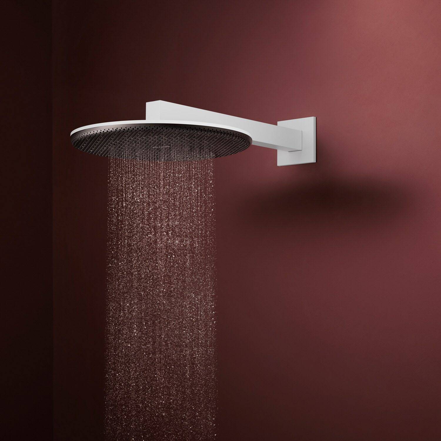 Moderner runder Regenduschkopf mit Wasser, das von einem wandmontierten Chromarm gegen einen dunkelroten Hintergrund herabströmt.