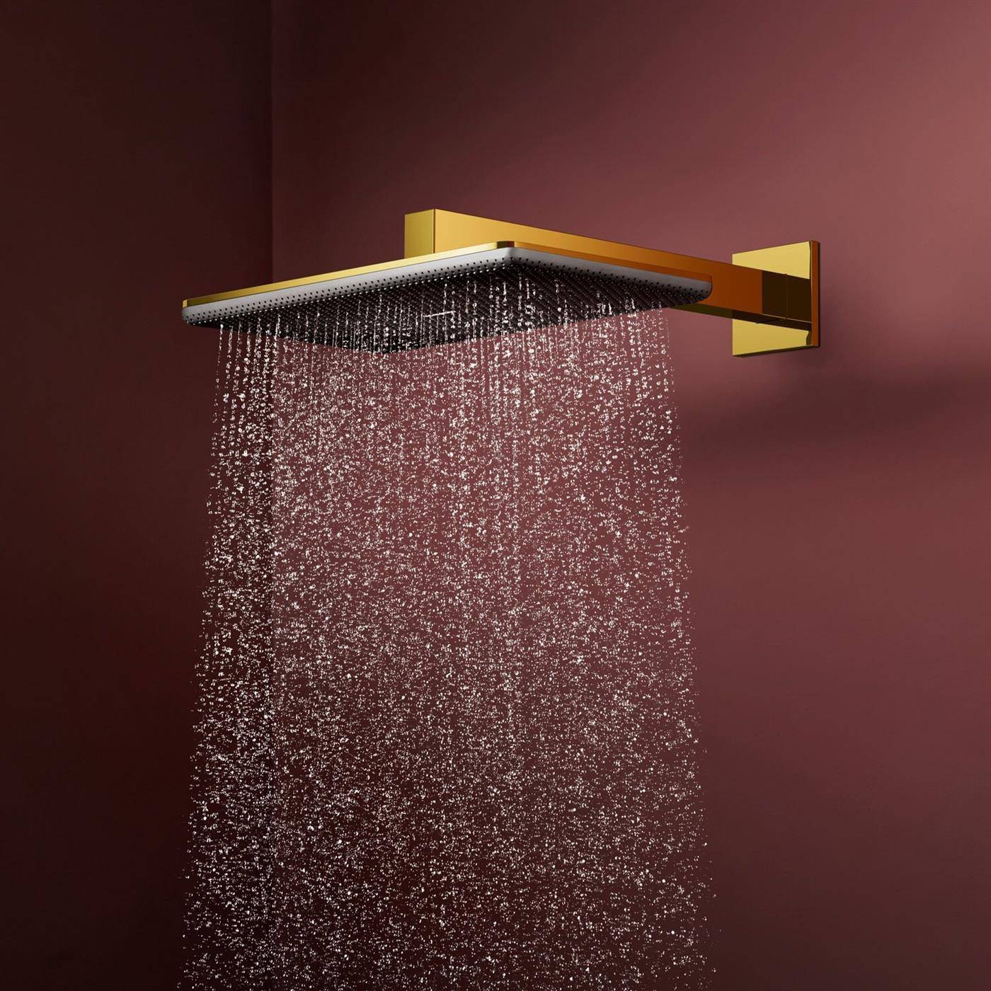 Goldener an der Wand montierter Regenduschkopf, der Wasser gegen einen dunkelrot gefärbten Hintergrund sprüht.