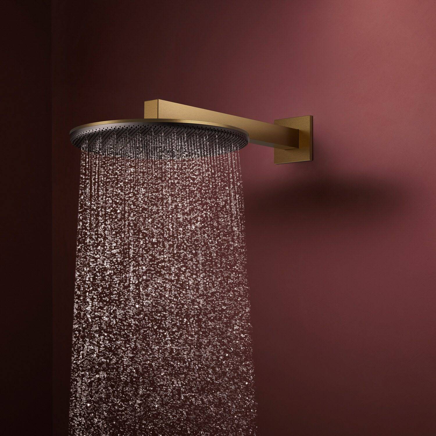 Runder goldener Regenbrausekopf an einer burgunderfarbenen Wand montiert, der einen gleichmäßigen Wasserstrom sprüht.