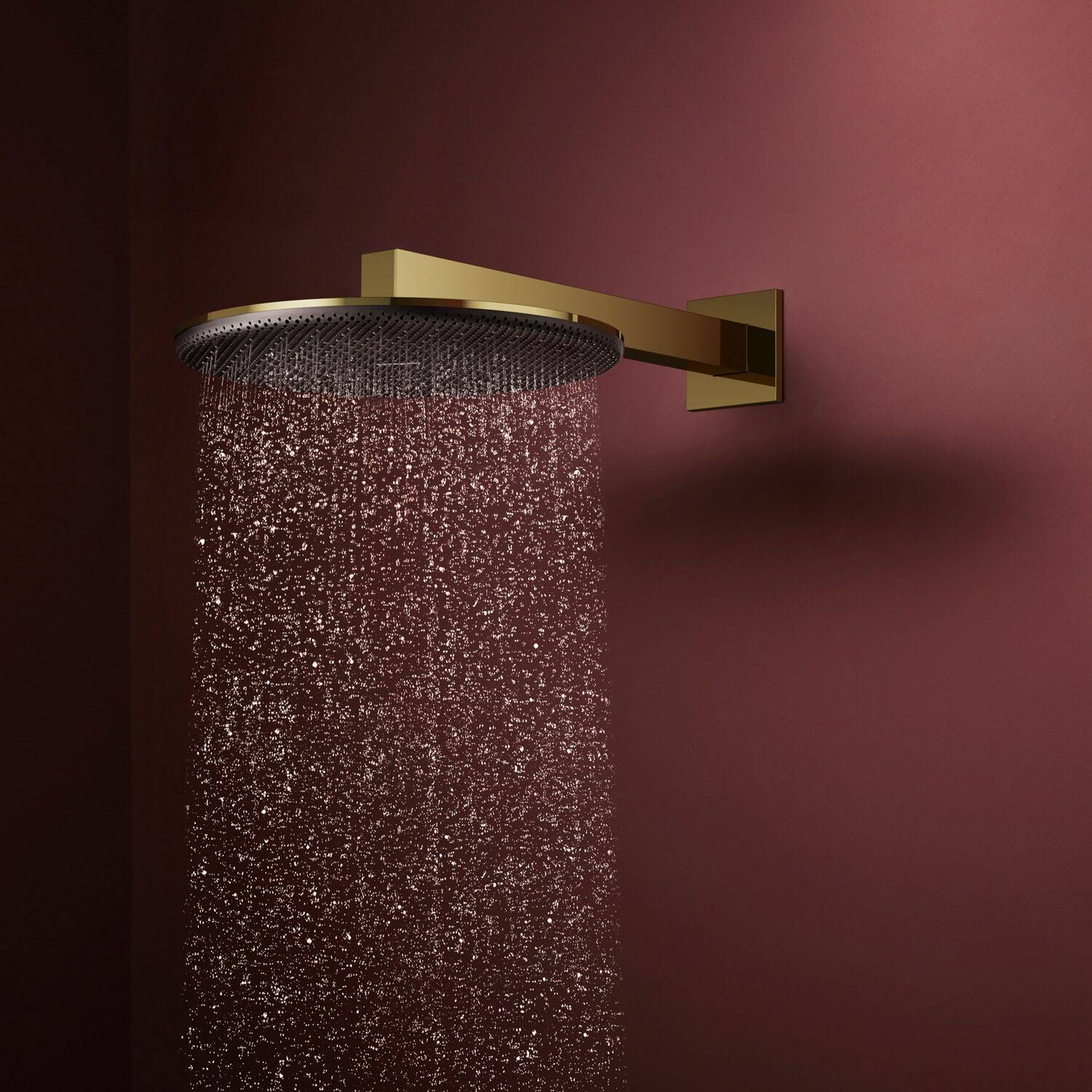 Goldene Regenduschkopf auf einer burgunderrotgewölbten Wand montiert, der Wasser in einem feinen Strahl nach unten sprüht.