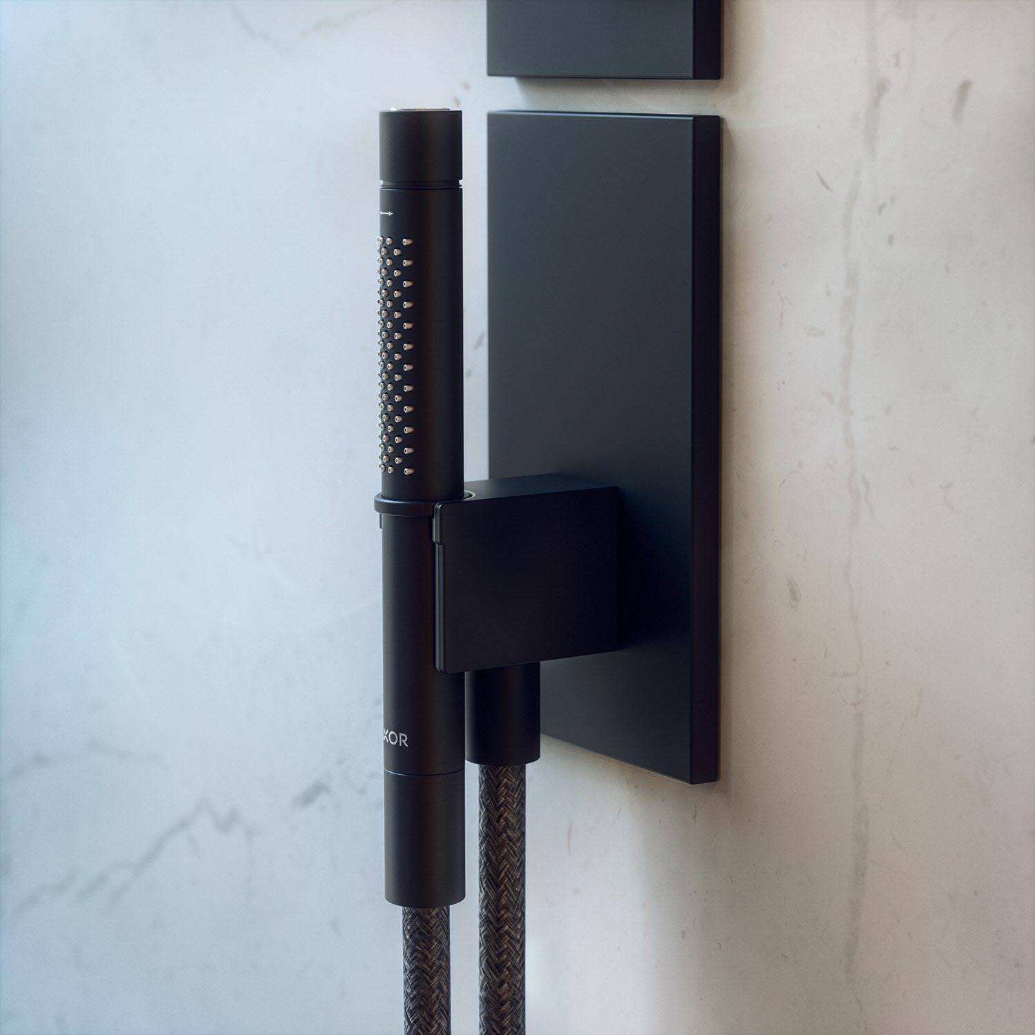 An der Wand montierte schwarze Handbrause mit Flechtschlauch und quadratischem Halter vor einer hellen Steinbadezimmerwand.