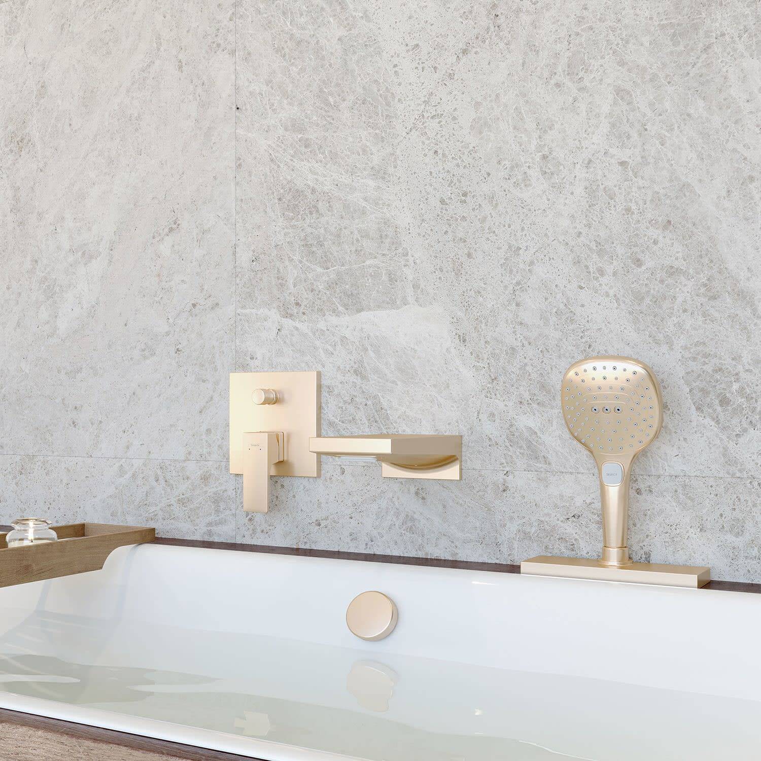 Modernes Badezimmer mit einer weißen Badewanne, vergoldetem Wandwasserhahn und entsprechender Handbrause vor einer hellgrauen Steinwand.