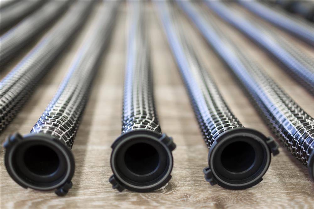 Nahaufnahme von vier aufgerollten metallischen flexiblen Schläuchen, die auf einer Holzoberfläche aneinander gereiht sind, aus der Perspektive der offenen Enden betrachtet.
