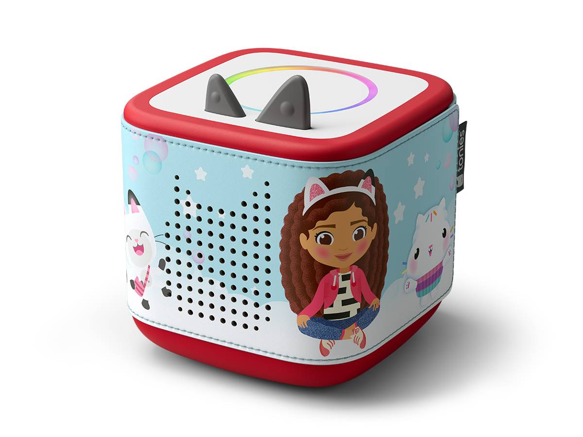Würfelförmiger Spielzeuglautsprecher mit Cartoon-Mädchen- und Katzengrafiken, roten Rand, perforierter Frontgitterabdeckung und zwei grauen ohrähnlichen Schaltflächen oben.
