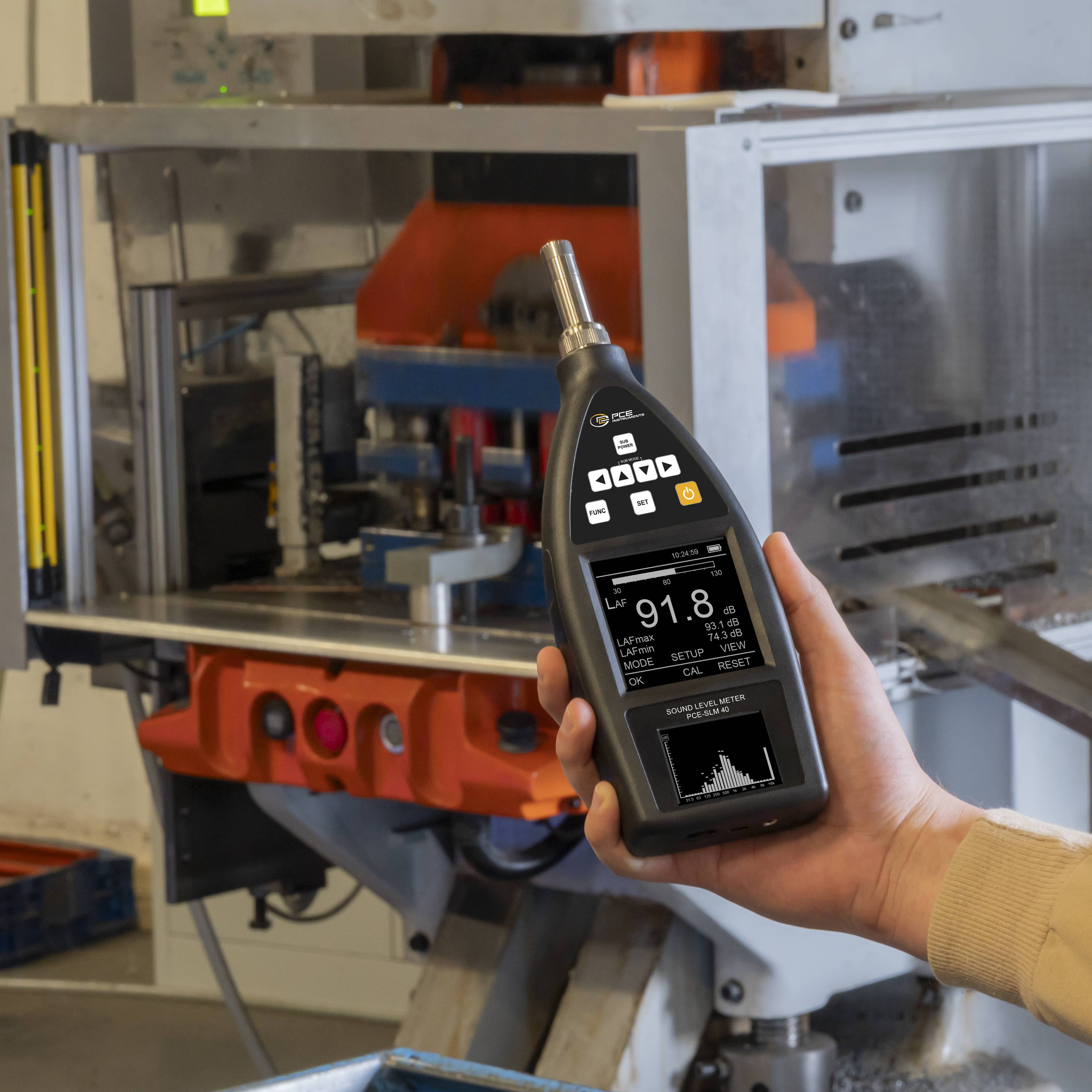 Hand, die ein digitales Schallpegelmessgerät vor einer Industriemaschine hält und einen Messwert von 91,8 dB anzeigt.