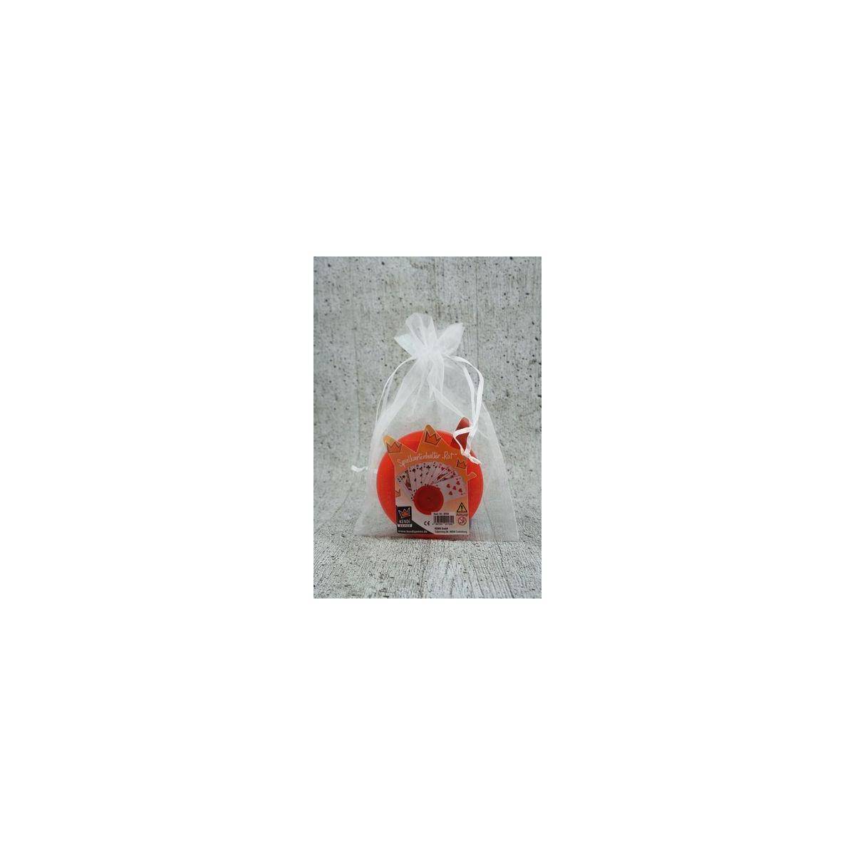 Ein kleines rot verpacktes Artikel in einer weißen Organza-Geschenktasche sitzt vor einem grauen Betonhintergrund.