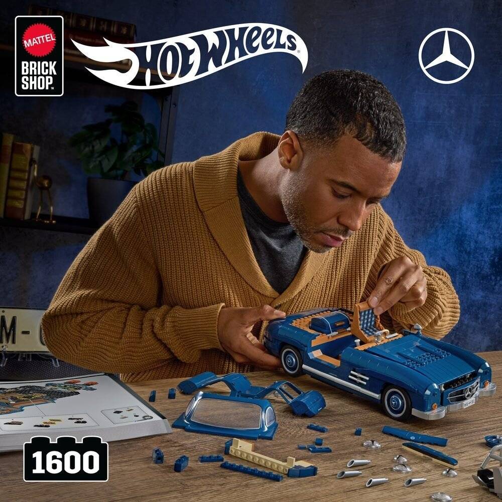 Ein Mann, der ein blaues Hot-Wheels-Mercedes-Benz-Modellauto aus 1600 Brick-Shop-Teilen an einem Tisch zusammensetzt, mit sichtbaren Hot-Wheels-, Mattel-Brick-Shop- und Mercedes-Logos.