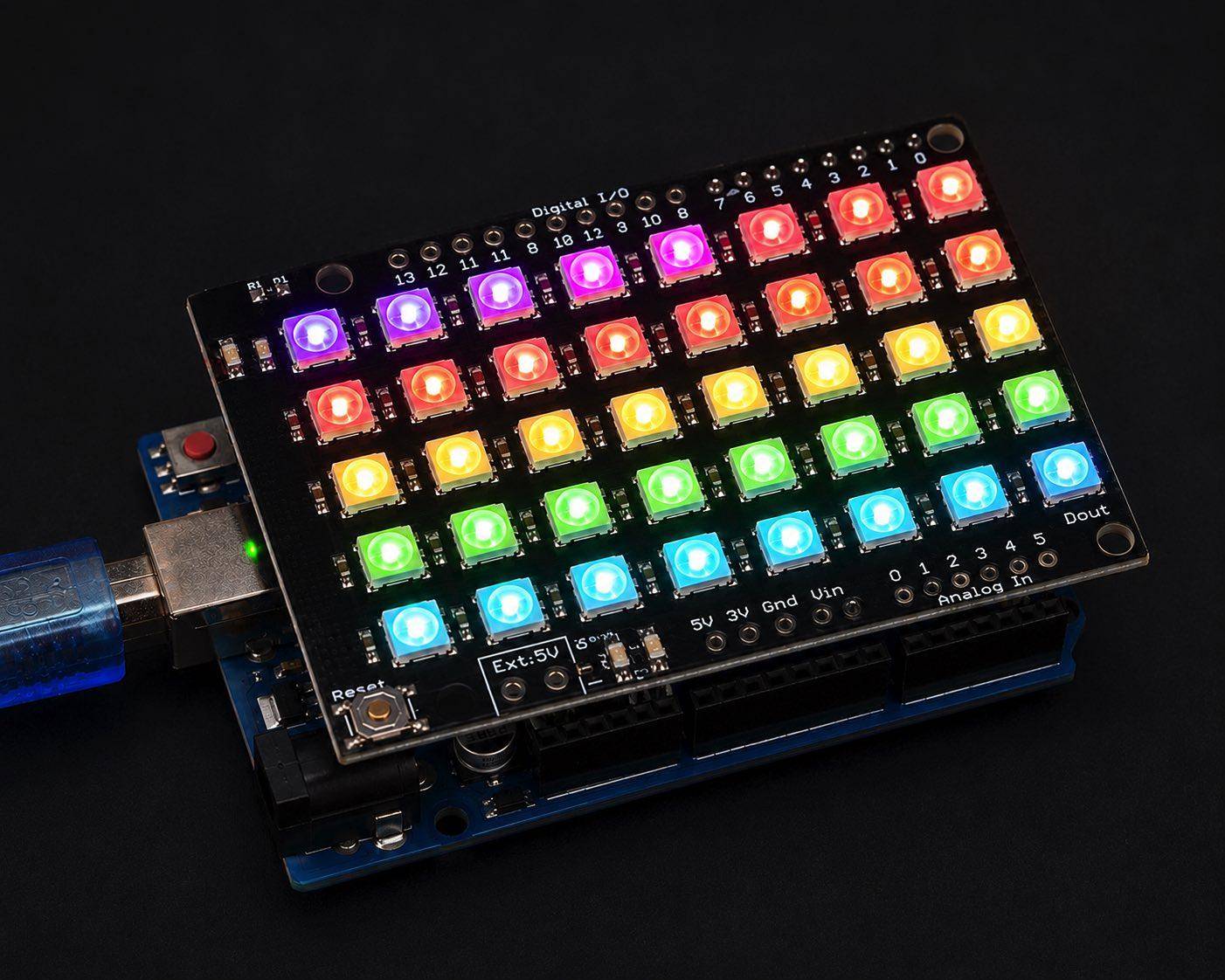 Ein über USB verbundenes Arduino-Board mit einem farbenfrohen LED-Matrix-Shield, das in Reihen von violetten, roten, gelben, grünen und blauen Lichtern erleuchtet ist.