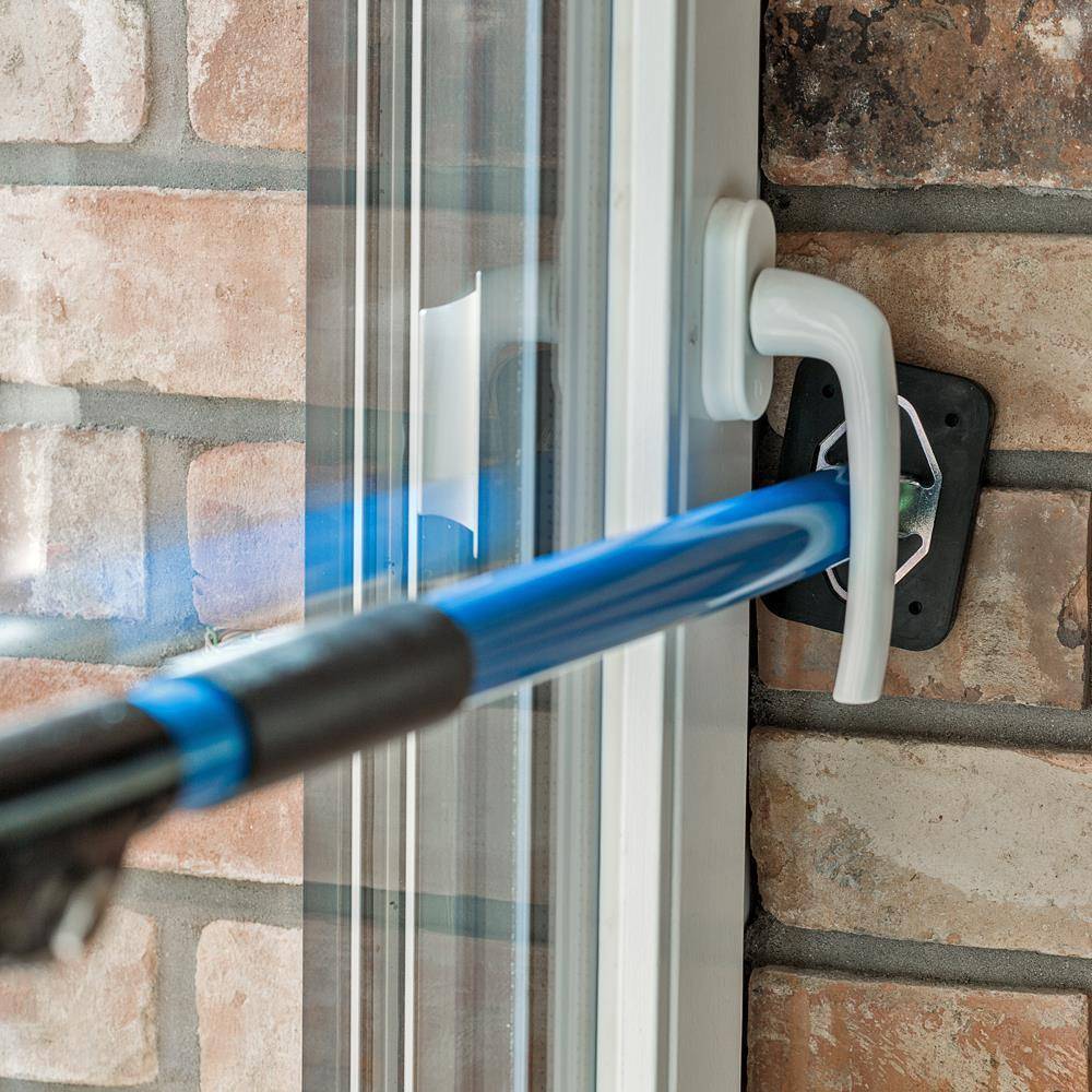 Blauer teleskopischer Fensterreinigungsstab mit einer Gummiabzieher, die gegen einen Glasschiebetürrahmen und eine Backsteinwand gepresst ist.