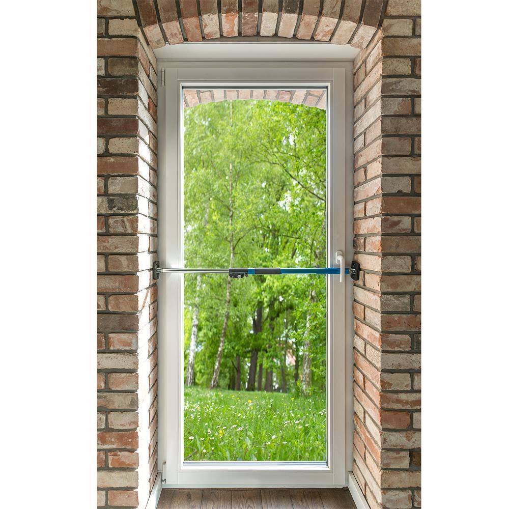 Eine weiße Stormtür in einer Ziegeleingangstüre wird durch einen horizontalen Sicherheitsriegel geschlossen, mit einem grünen Waldgarten, der außen sichtbar ist.