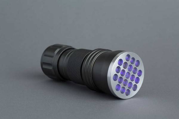 Eine schwarze Taschenlampe liegt auf ihrer Seite und zeigt eine runde Vorderseite mit mehreren violetten LED-Glühbirnen vor einem grauen Hintergrund.