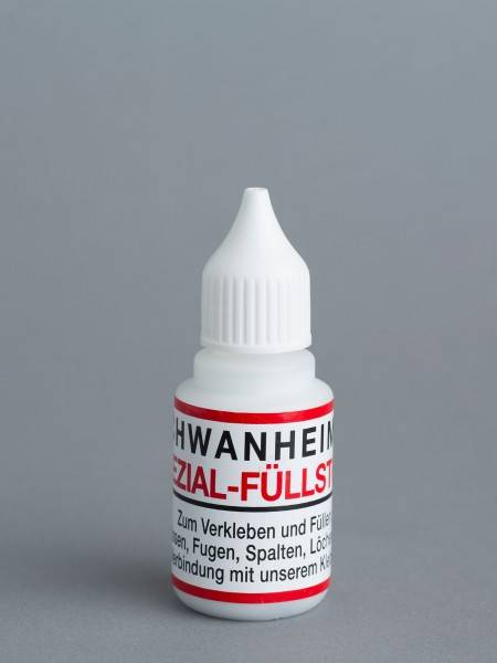 Kleine weiße Kunststoff-Quetschflasche mit spitzer Kappe und deutschem Etikett, wahrscheinlich Kleber oder Füllstoff, auf grauem Hintergrund.
