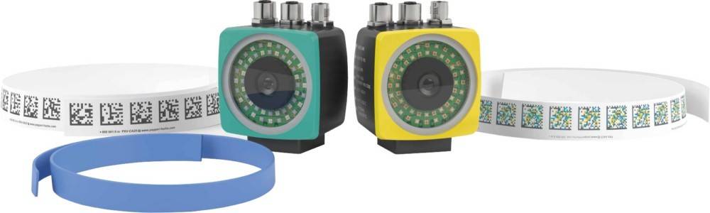 Zwei industrielle Kameramodule, eines in Türkis und eines in Gelb, neben einem blauen Kabel und zwei Rollen mit bedrucktem Musterstreifen.