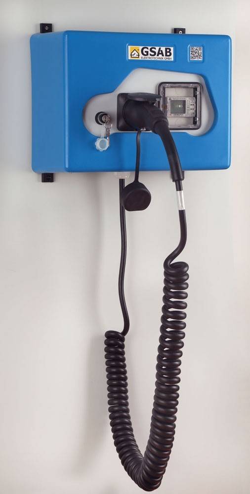 Blaue GSAB-Elektrofahrzeug-Ladestation mit angeschlossenem Ladestecker und aufgewickeltem Kabel an der Wand montiert.