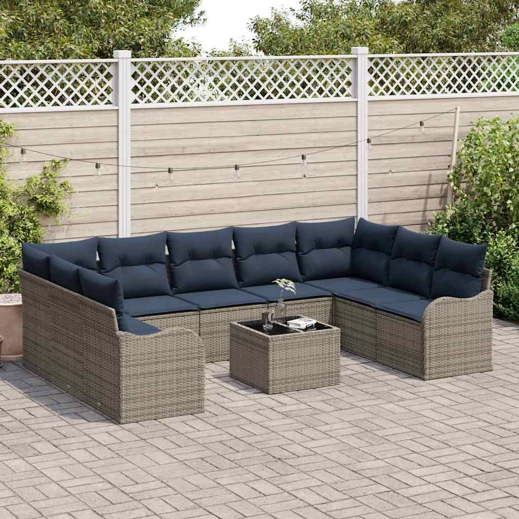Outdoor L-förmiges Rattansofa mit dunklen Kissen um einen quadratischen Couchtisch auf einer gepflasterten Terrasse neben einem Zaun und Grünflächen.