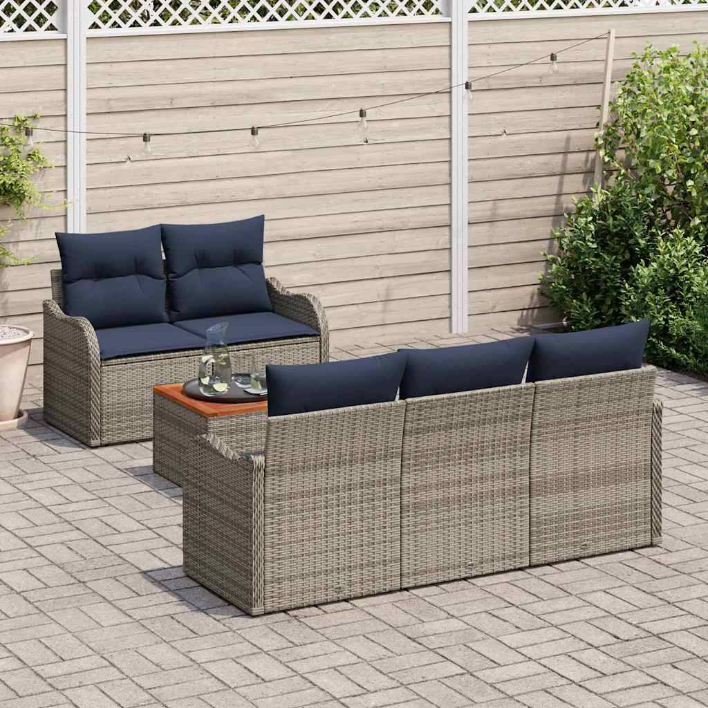 Terrasse im Freien mit geflochtenem Rattan-Ecksofa, dunklen Kissen und einem kleinen Tisch auf einer gepflasterten Terrasse neben einem Holzzaun und Grünflächen.