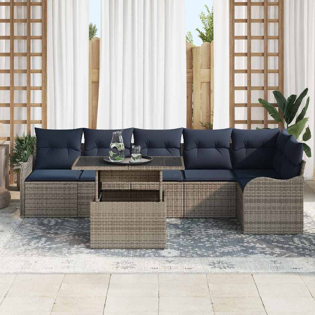 Outdoor-Rattangarnitur mit marineblauen Kissen und einem Glastisch auf einem gemusterten Teppich in einer Terrassensetting.