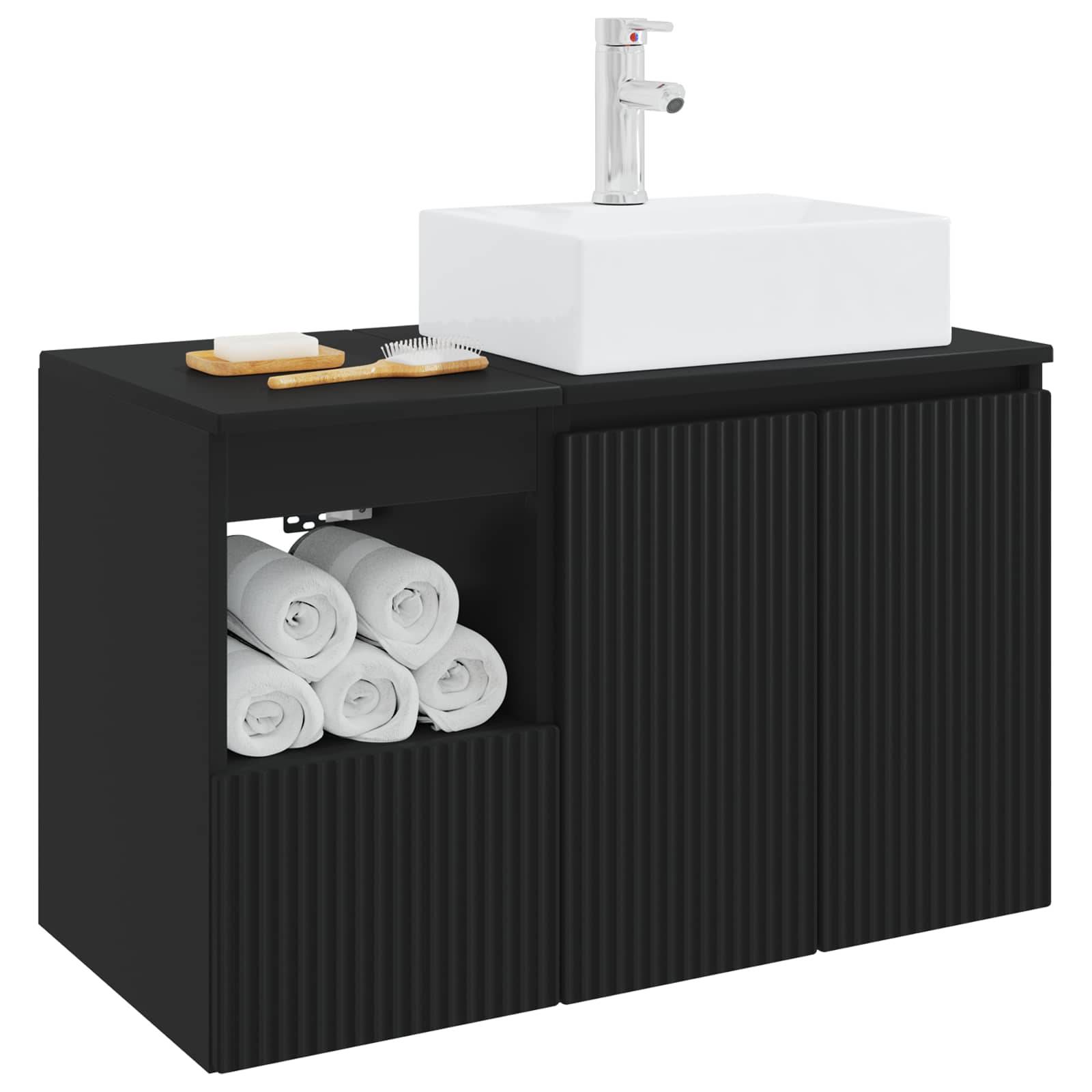 Schwarzes Badezimmermöbel mit weißem Waschbecken und Armatur, offenes Regal mit aufgerollten Handtüchern und Arbeitsplattenzubehör auf der linken Seite.