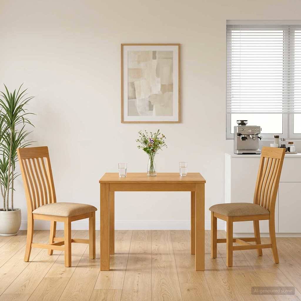Minimalistischer Essbereich mit zwei Holzstühlen, einem kleinen Tisch mit Blumen und Gläsern, gerahmter Wandkunst, einer Topfpflanze und einer Küchenzeile mit einer Kaffeemaschine neben einem Fenster.