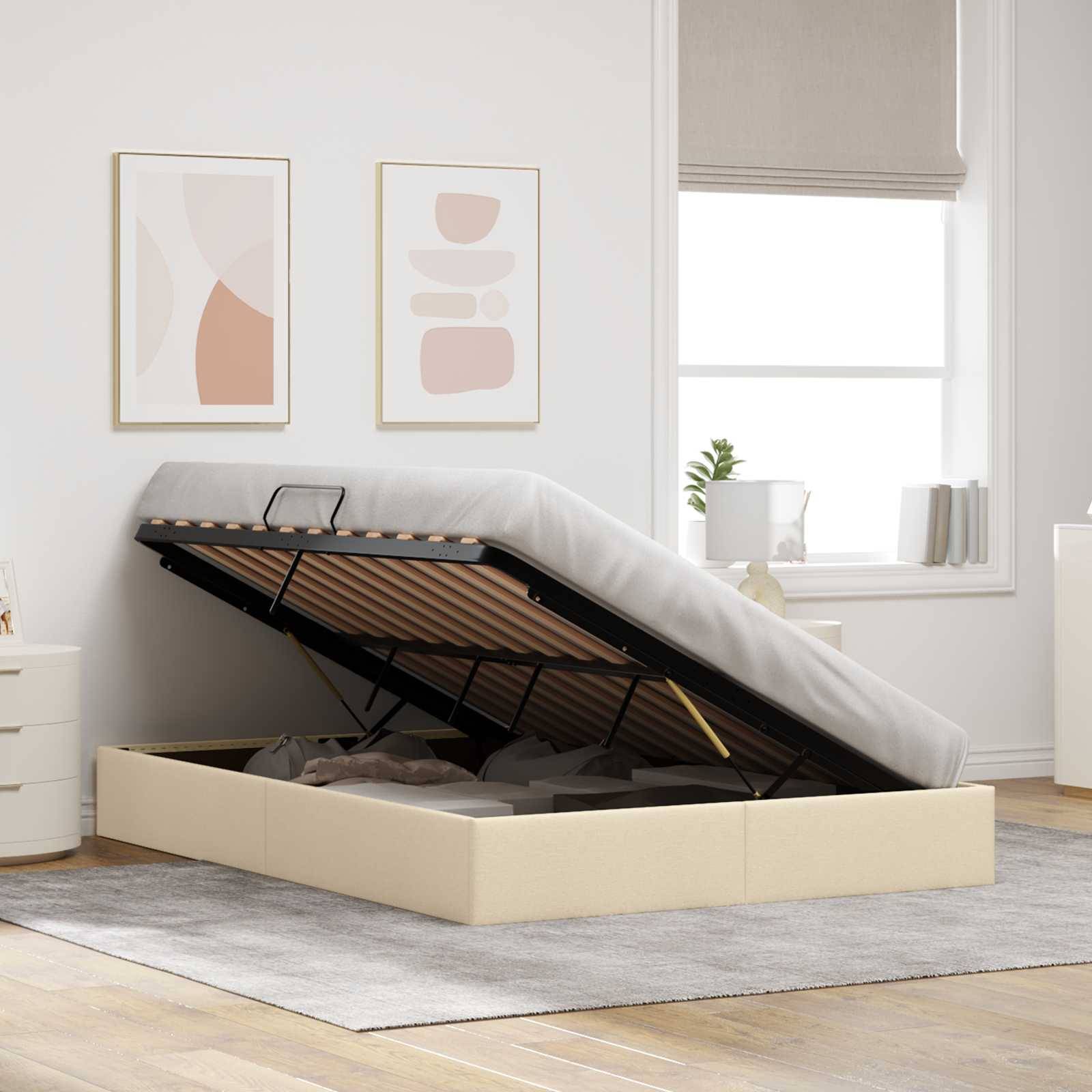 Beige gepolstertes Ottomane-Bett mit angehobenem Matratzenlager, das ein Stausfach offenbart, in einem hellen Schlafzimmer neben einem Fenster und einer Wandkunst.