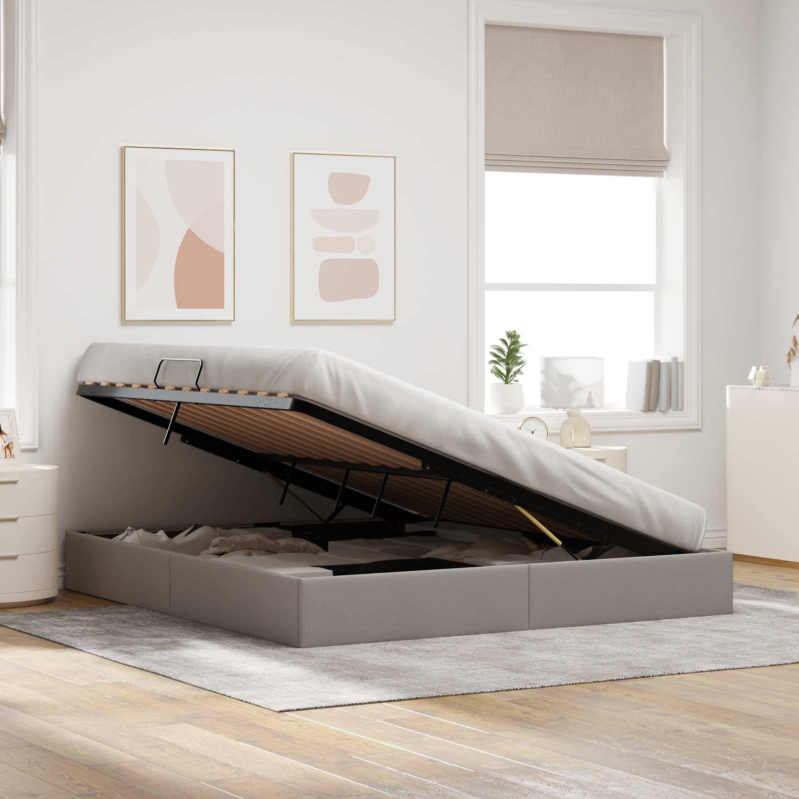 Ein gepolstertes Speicherbett wird geöffnet und zeigt das Unter-Bett-Fach in einem hellen Schlafzimmer mit gerahmten Wandbildern und einem Fenster.