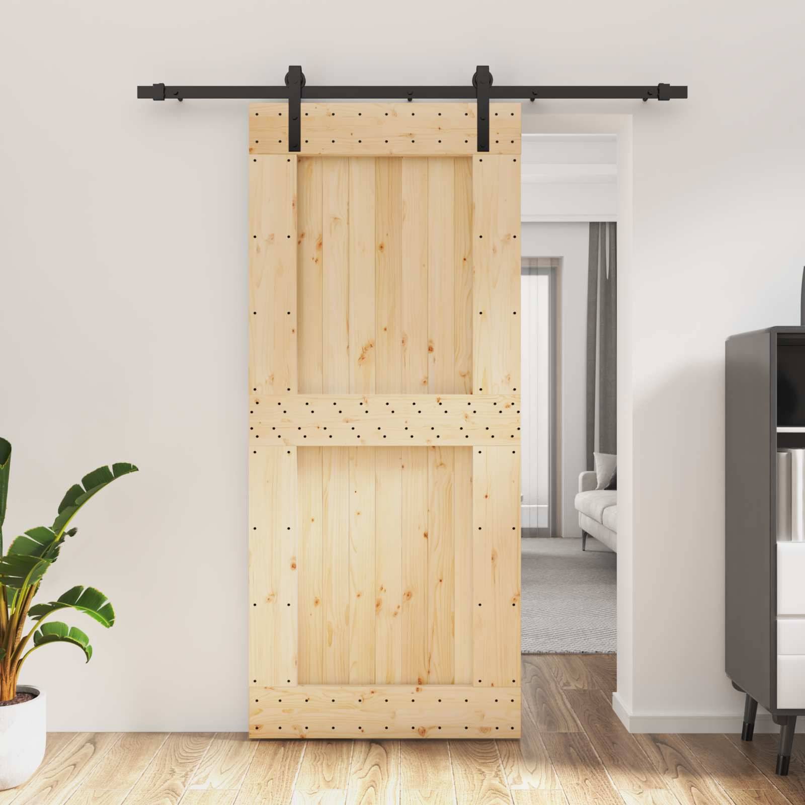 Holzschiebertor teilweise verdeckt eine Türöffnung mit einer schwarzen Metallschiene und einem Blick auf ein Wohnzimmer dahinter.